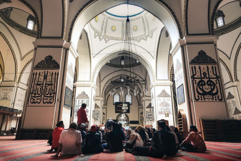 People sitting inside Bursa's Grand Mosque, showcasing stunning Islamic architecture and ornaments.